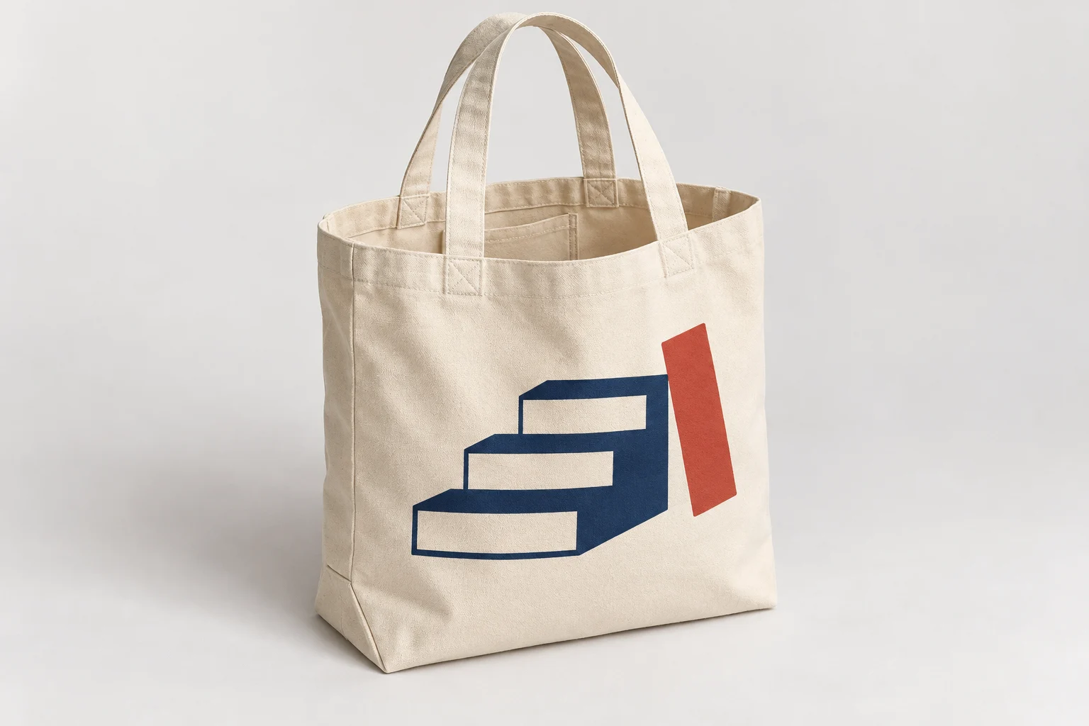 Cream canvas tote with a large blue stepped-page graphic, red rectangular accent and two plain handles